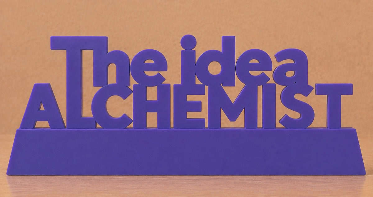 Concept render: stacked desk sign reading The Idea Alchemist